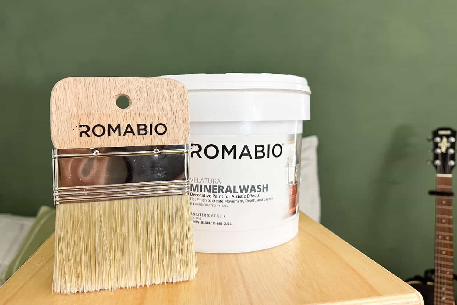 bucket of Romabio velatura mineralwash and spalter brush in front of green limewashed wall