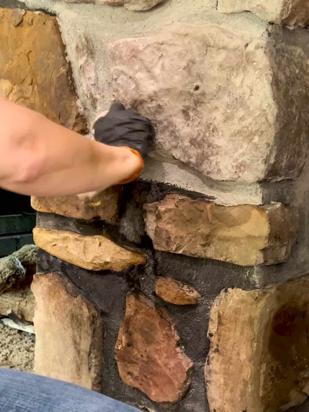 A person is painting a stone wall with a rag.