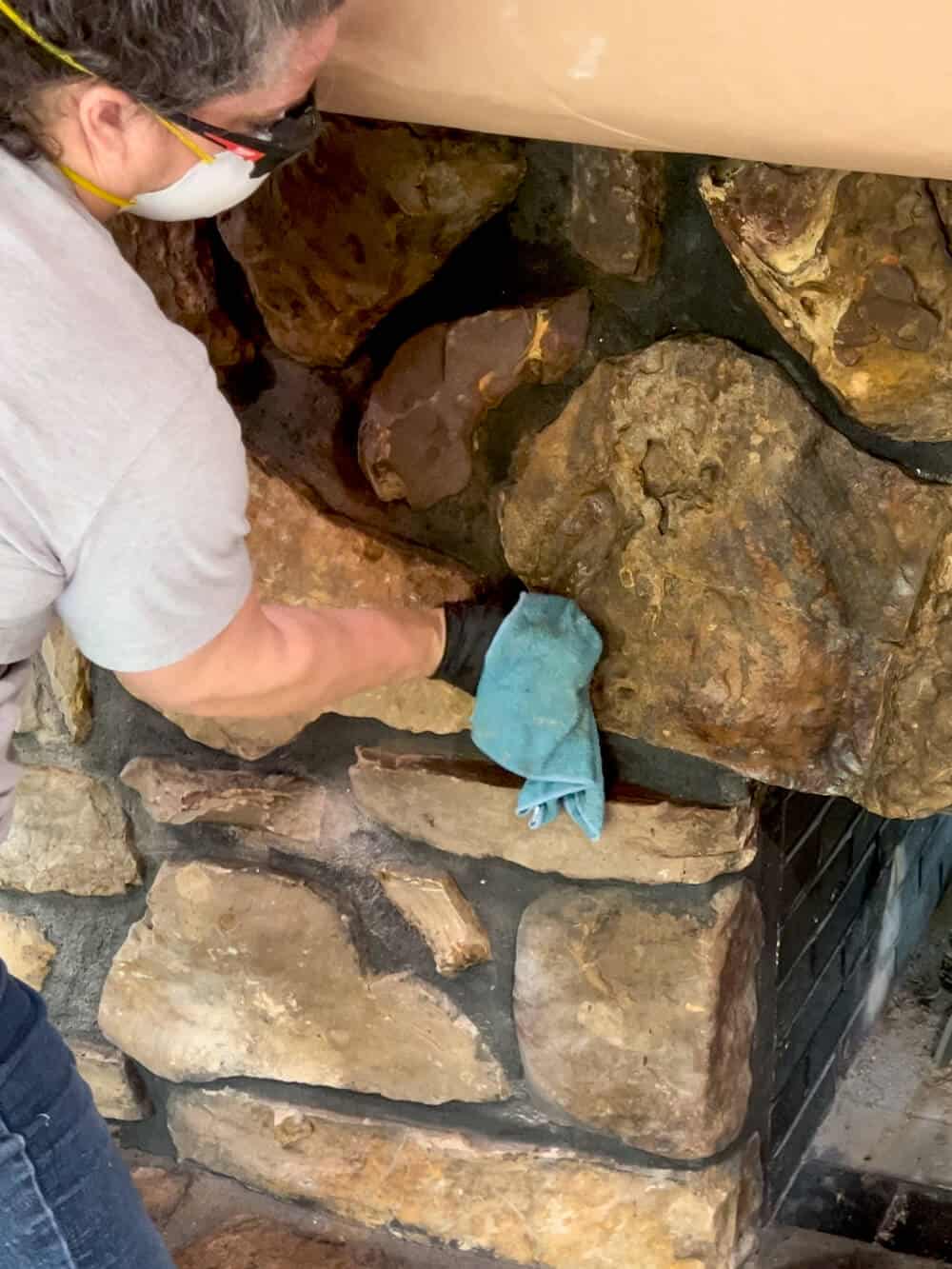 A woman wearing gloves and a mask is cleaning a stone fireplace.