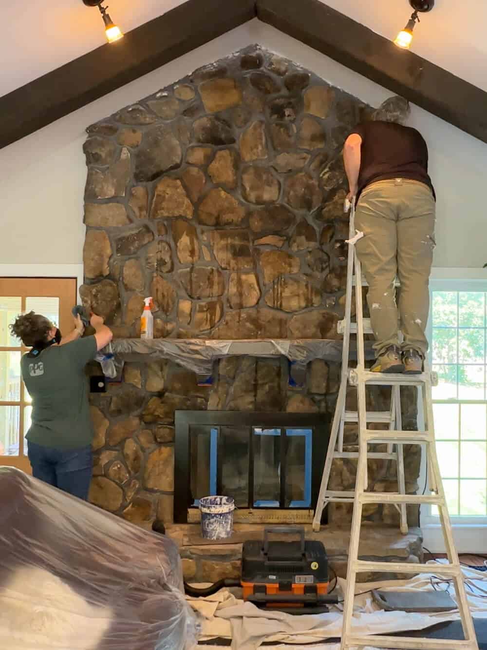 Two people working on a stone fireplace in a home.