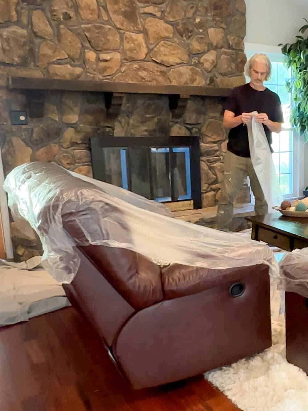 A man is wrapping a couch in plastic.